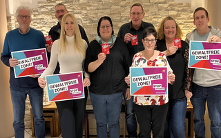 Eine Gruppe Menschen hält Schilder gegen Gewalt an Frauen in die Kamera